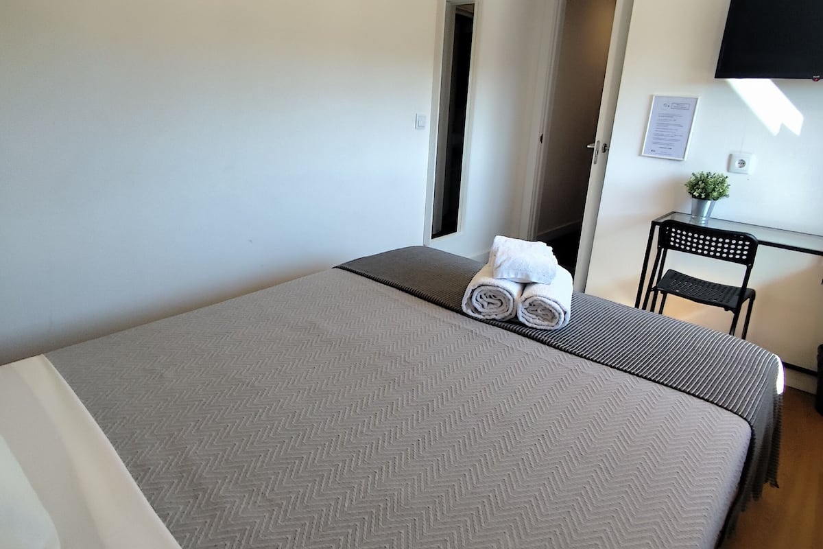 A hotel room with a large bed, a desk, a chair, and a TV mounted on the wall.
