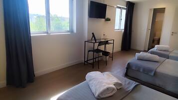 A hotel room with two beds, a desk, a TV, and a window with curtains.