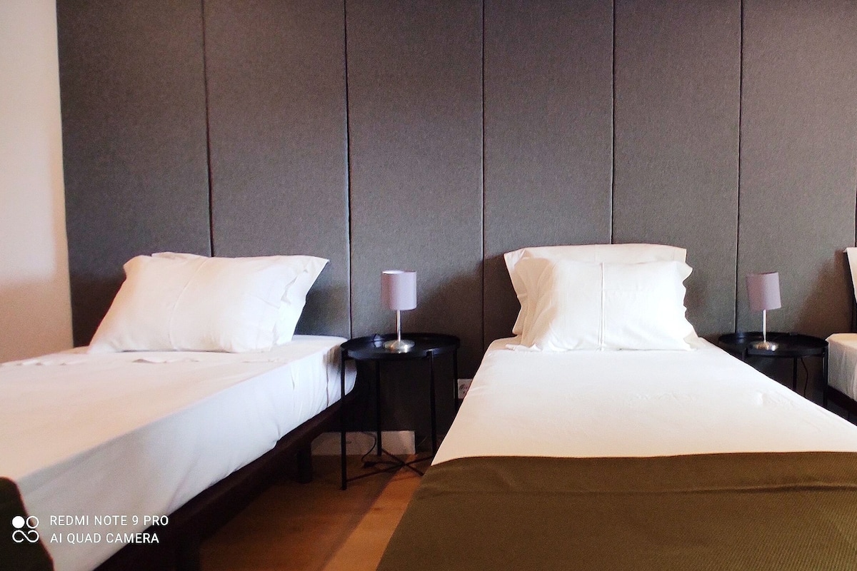A hotel room with two single beds, a large bed, and a nightstand with a lamp.