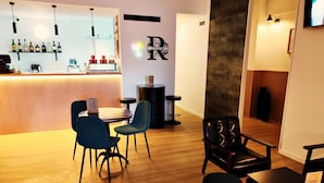 A bar area with a counter, shelves with bottles, and a neon sign. There are chairs and tables in the foreground. - Residencial Douro (Peso da Régua)