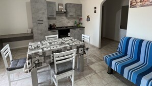 A modern kitchen with grey cabinets, a dining table with chairs, and a striped sofa. - VILLA MACCIONI 2  (Tanaunella)