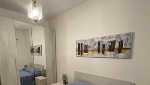 A bedroom with a bed, a nightstand, a lamp, a mirror, and a painting on the wall. - VILLA MACCIONI 2  (Tanaunella)