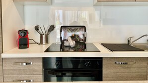 A modern kitchen with a built-in oven, a stainless steel range hood, and a window with a view of trees.