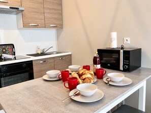 A modern kitchen with a microwave, sink, and a breakfast setup including croissants and red cups.