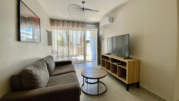 A living room with a sofa, a coffee table, a TV on a wooden stand, and a ceiling fan.