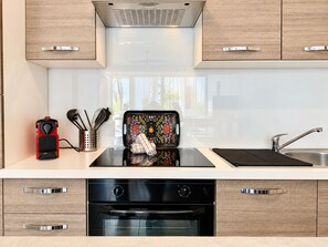 A modern kitchen with a built-in oven, a stainless steel sink, and wooden cabinets. - Rêves salés Appartement une chambre 4 couchages avec terrasse 17m2 plage (Le Grau-du-Roi)