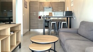 A modern living room with a sofa, two small tables, a TV, and a kitchen in the background.