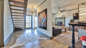 A spacious living area with a wooden staircase, a fireplace, and a large painting.