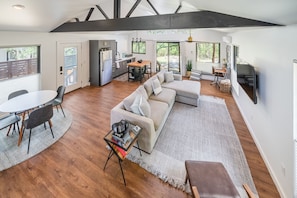 A spacious living area with a large sofa, a dining table, and a kitchen in the background. - Texas Retreat- Sunset Rock | Romantic Hideaway for Two (Wimberley)