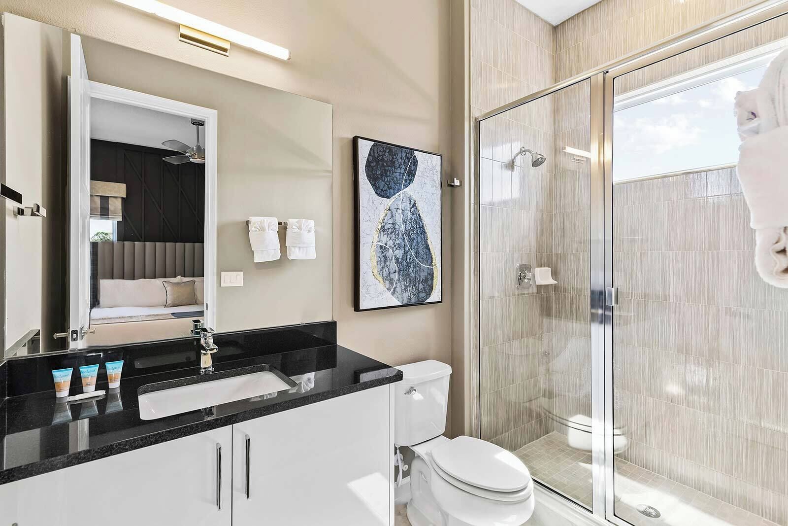 A modern bathroom with a glass shower enclosure, a black countertop sink, and a white toilet.
