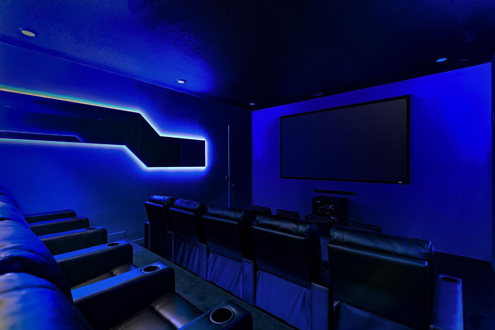 A home theater room with a curved seating arrangement, a large flat-screen TV, and a wall-mounted projector.