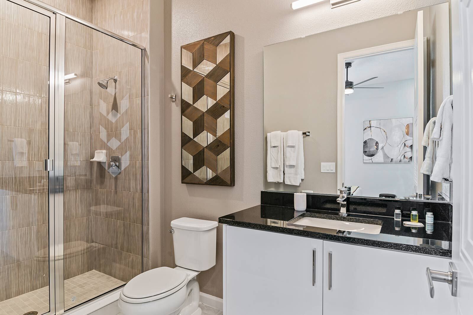 A modern bathroom with a glass-enclosed shower, a toilet, a vanity with a black countertop, and a mirror.