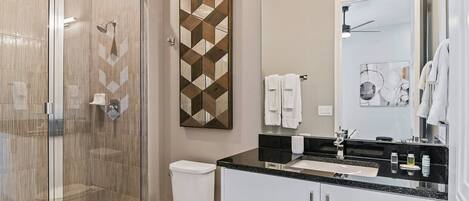 A modern bathroom with a glass-enclosed shower, a toilet, a vanity with a black countertop, and a mirror.