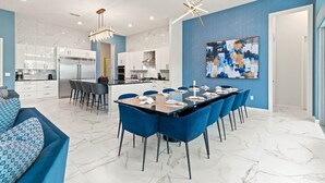 A modern kitchen with white cabinets, a dining area with blue chairs, and a large abstract painting on the wall. - Cozy Home w Treehouse RM, Bowling Arcade, Theater, Castle Theme BR, Near Disney (Davenport)