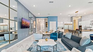 A modern living room with a sofa, chairs, a coffee table, and a kitchen area in the background. - Cozy Home w Treehouse RM, Bowling Arcade, Theater, Castle Theme BR, Near Disney (Davenport)