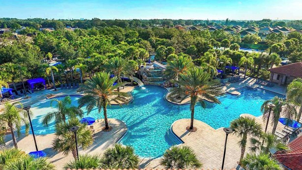 A resort with a large central pool surrounded by palm trees and lounge chairs. - Cozy Home w Treehouse RM, Bowling Arcade, Theater, Castle Theme BR, Near Disney (Davenport)