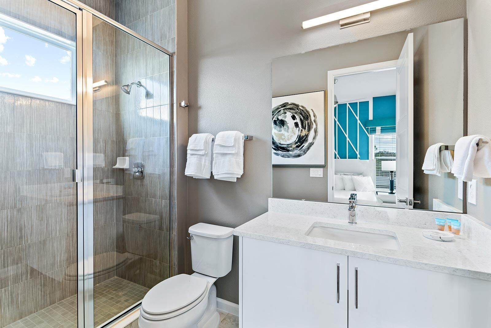 A modern bathroom with a glass shower enclosure, a white toilet, a large mirror, and a marble sink.