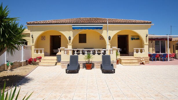 A building with a tiled roof, a covered patio with chairs, and a small garden area. - Casa Mari is a fabulous Villa with large swim pool, tennis,  Games Room, garden  (Turre)