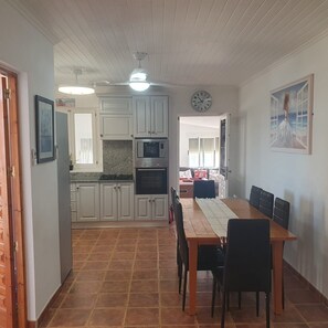 A kitchen with white cabinets, a microwave, and an oven. There is a dining table with chairs and a clock on the wall.