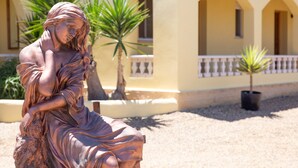 A bronze statue of a seated figure with a contemplative expression, set against a building with arched windows and a tiled roof. - Casa Mari is a fabulous Villa with large swim pool, tennis,  Games Room, garden  (Turre)