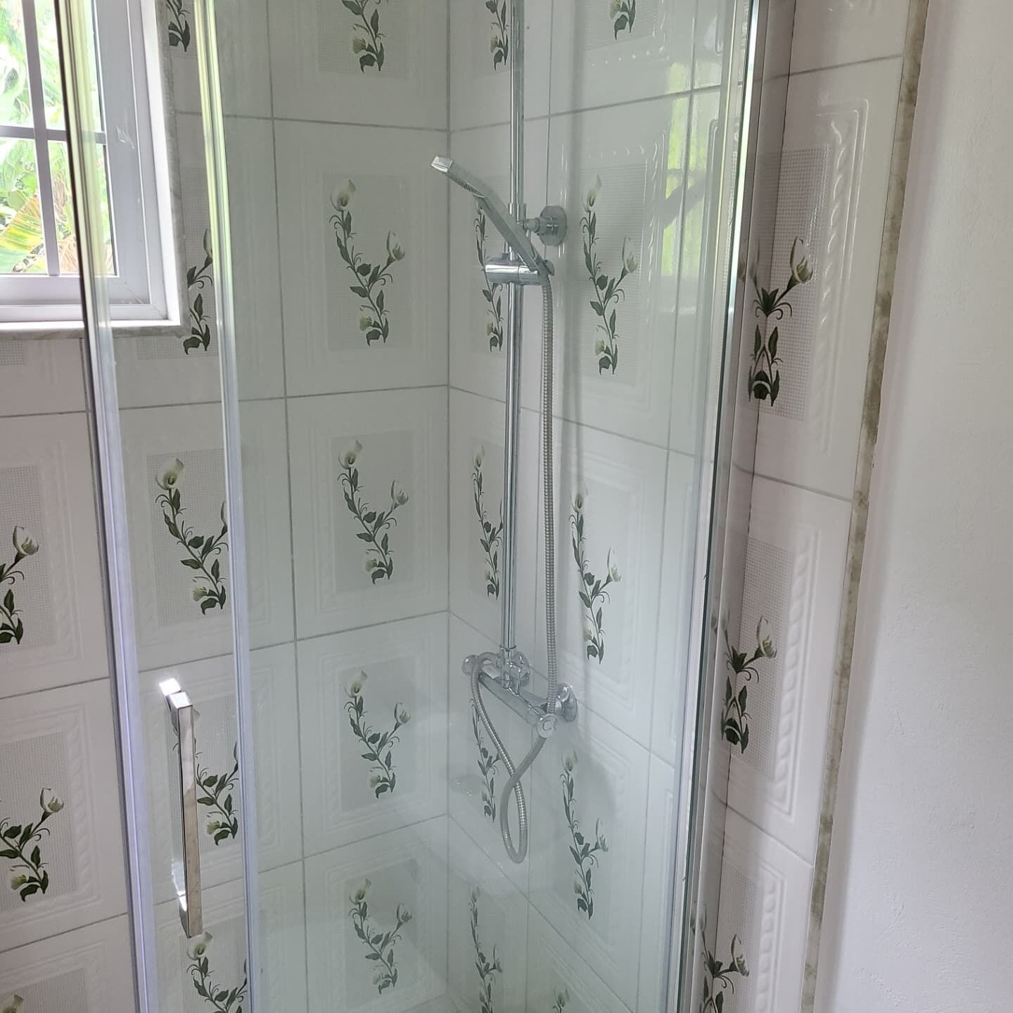 Una ducha con cerramiento de vidrio, cabezal de ducha manual y llave de pared.