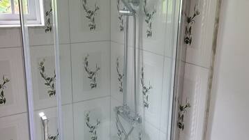 Una ducha con cerramiento de vidrio, cabezal de ducha manual y llave de pared.