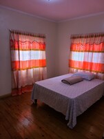 A bedroom with a bed, curtains, and wooden flooring.