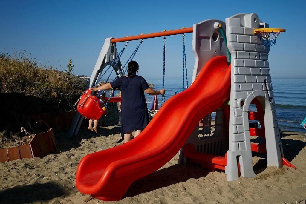 Une aire de jeux avec un toboggan rouge et des balançoires sur une plage de sable.