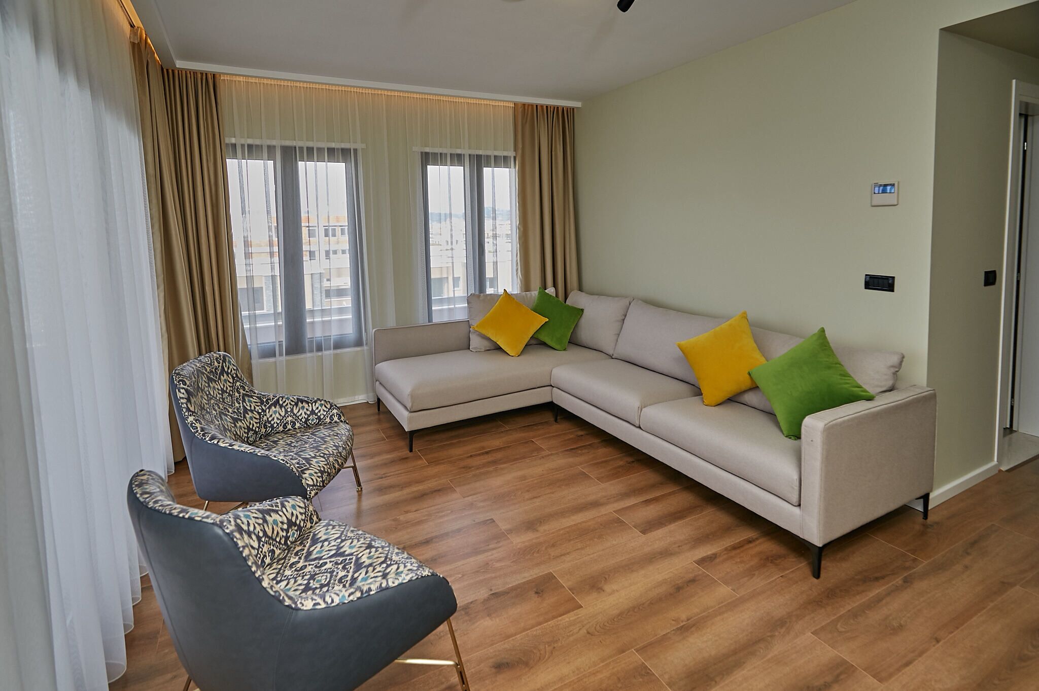 A modern living room with a beige sofa, two patterned armchairs, and a wooden floor.
