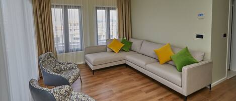A modern living room with a beige sofa, two patterned armchairs, and a wooden floor.