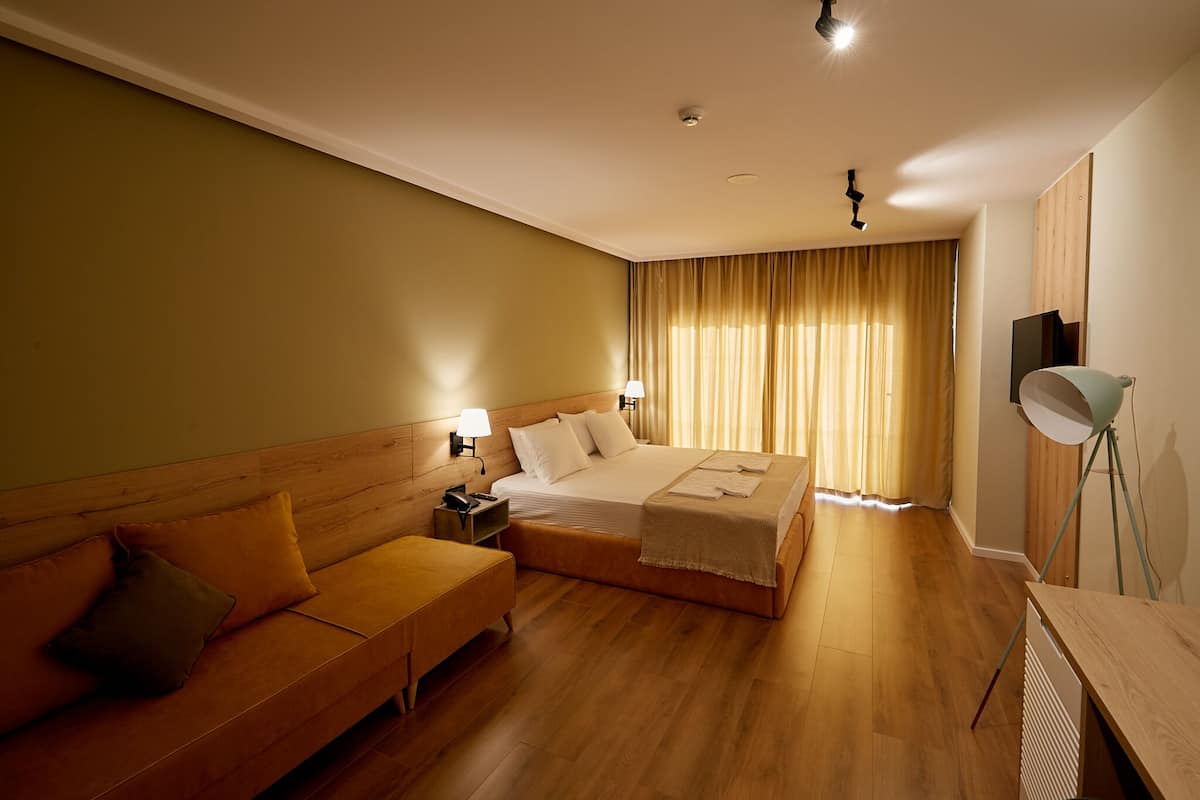 A hotel room with a large bed, a wooden headboard, a sofa, a desk, and a lamp.