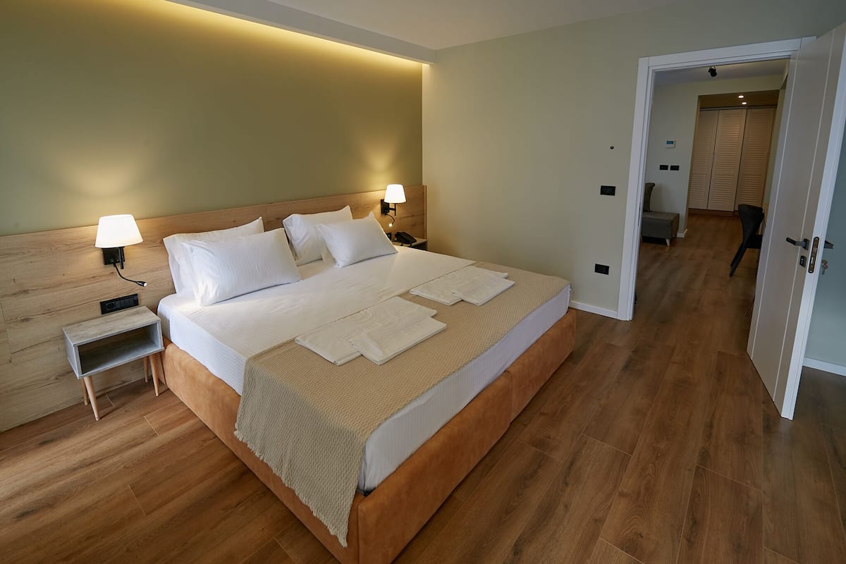 A neatly made bed with white linens and a beige throw blanket, two bedside lamps, a wooden nightstand, and a wooden headboard.