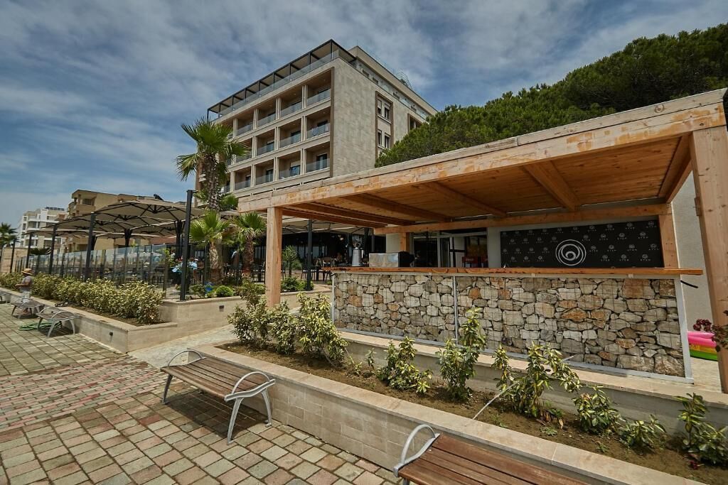 A modern building with a covered outdoor area, stone walls, and a paved walkway with benches.
