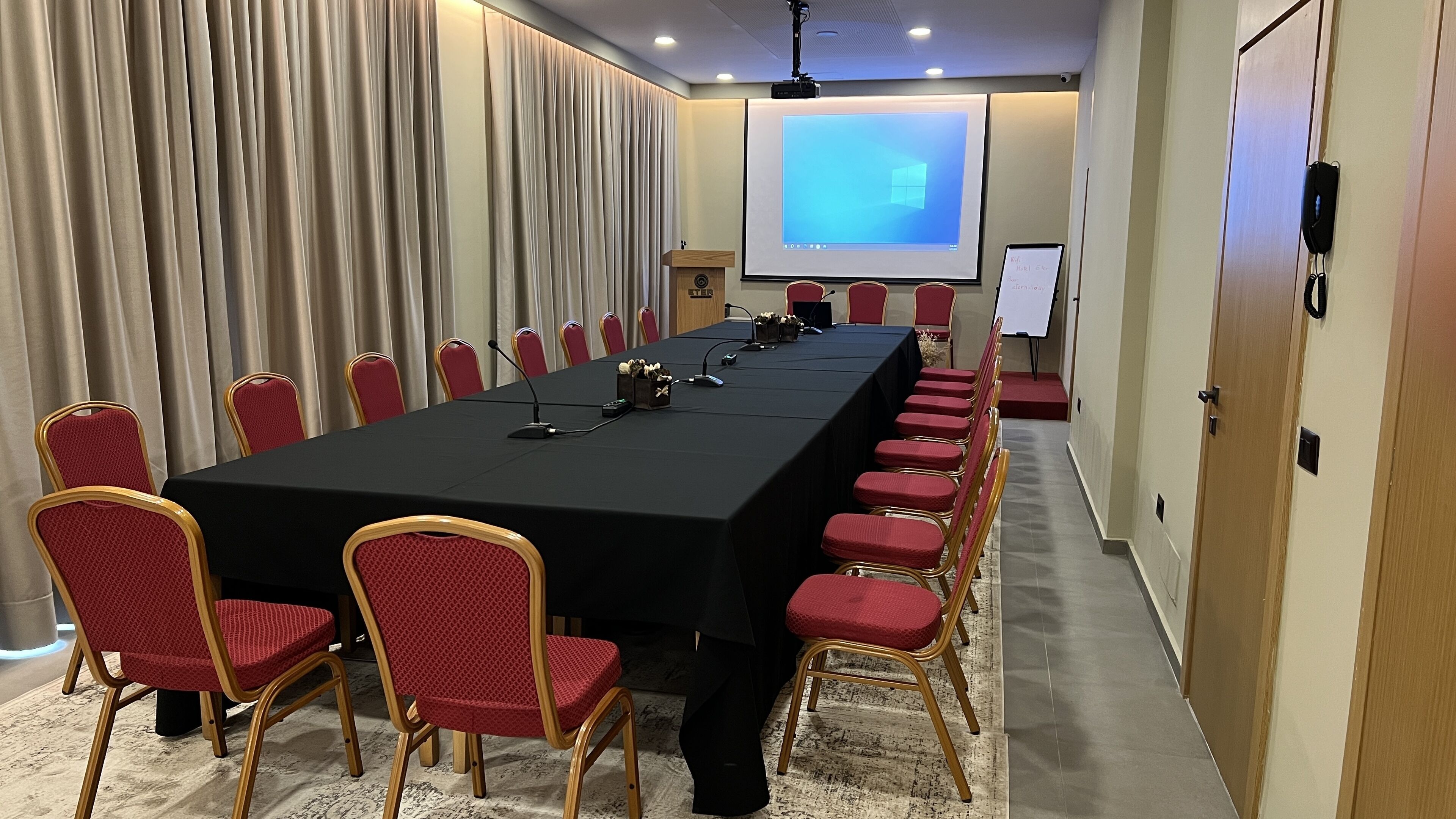 Une salle de conférence avec une longue table, des chaises rouges, un écran de projection et un tableau blanc.