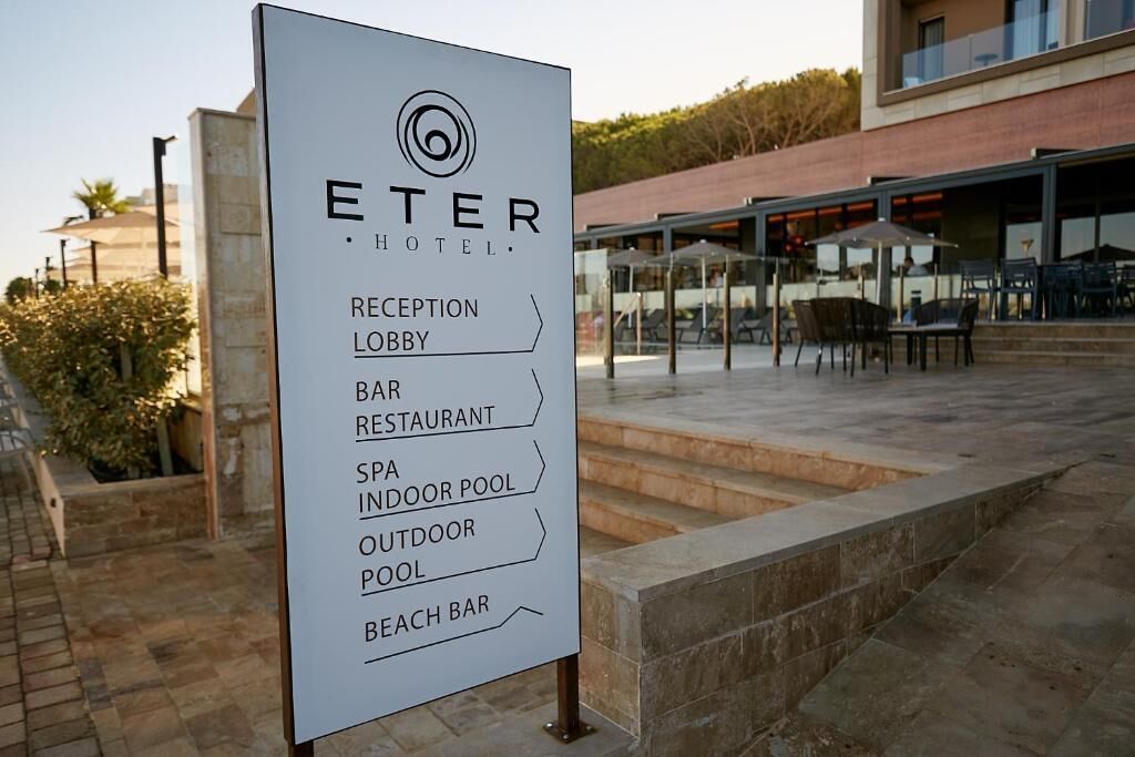 Segnaletica dell'Hotel ETER che indica servizi come hall della reception, bar, ristorante, spa, piscina coperta, piscina esterna e bar in spiaggia.