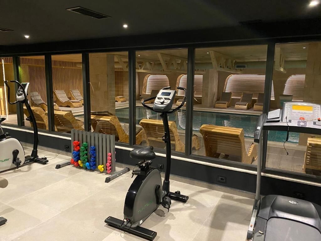 Un gimnasio con equipo de ejercicio, una piscina y sillones de madera.