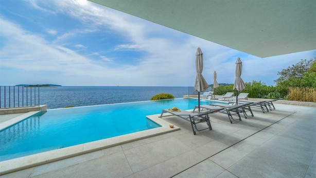 A private pool with lounge chairs and umbrellas, overlooking the sea.