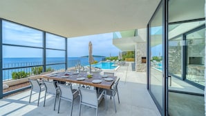 A dining area with a table set for four, overlooking a pool and the sea.
