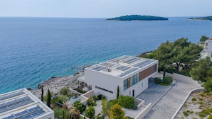 A modern building with a rooftop garden and solar panels, overlooking a coastal area with clear blue waters and a distant island.
