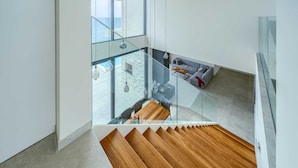 A modern interior with a glass staircase leading to a balcony overlooking a body of water.