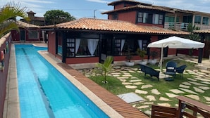 A swimming pool adjacent to a building with a tiled roof, outdoor seating, and a stone pathway.