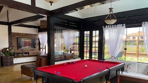 A pool table in a room with a TV, seating area, and large windows.