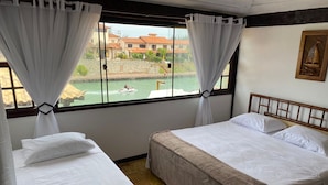 A room with two beds, white bedding, a view of a body of water, and a wooden headboard.