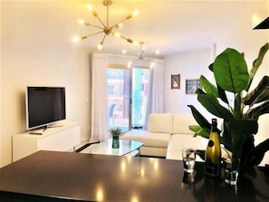 A modern living room with a flat-screen TV, a coffee table, a sofa, and a large plant.