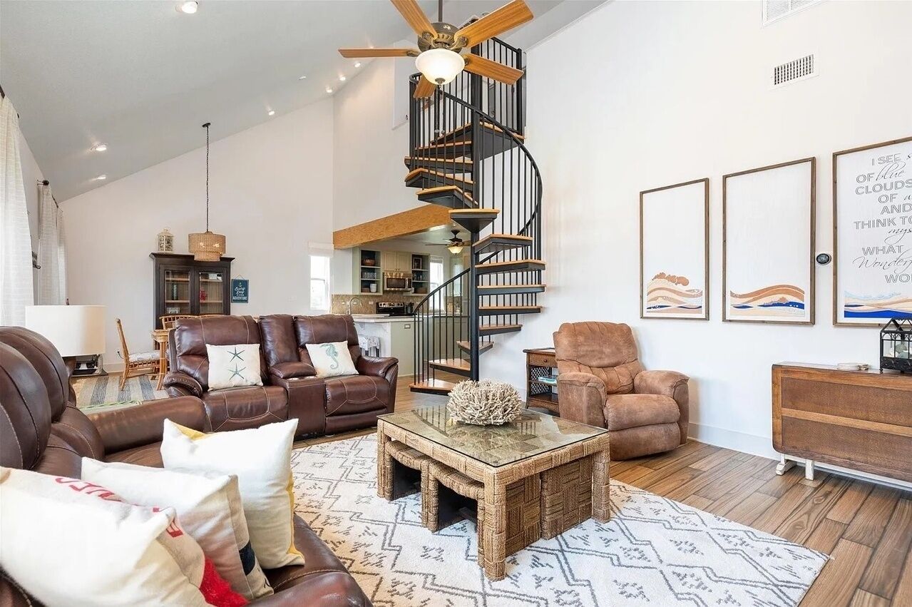 Ein geräumiges Wohnzimmer mit hoher Decke, einem Holztisch, Ledersofas und einer Wendeltreppe.