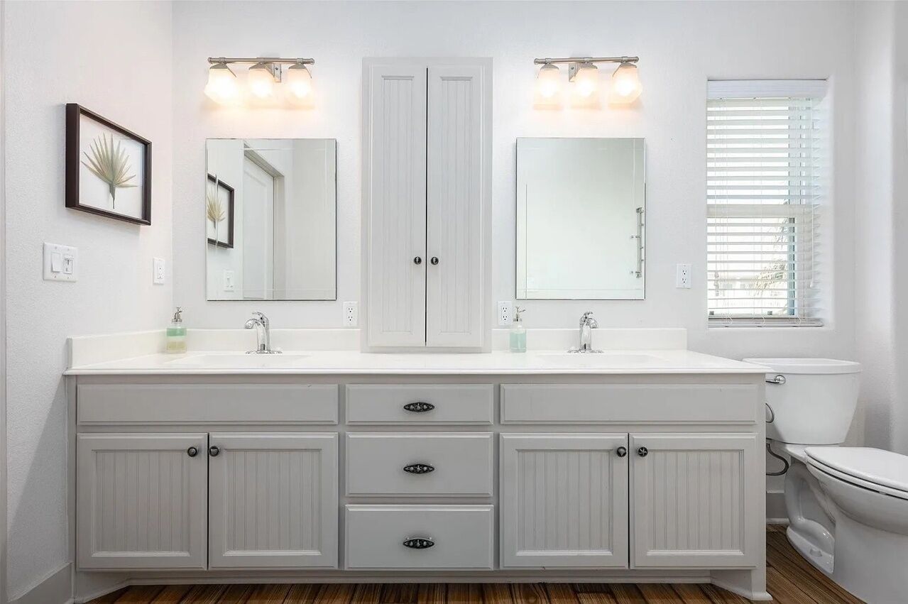 Een badkamer met een wit wastafelmeubel, dubbele wastafels en een toilet.