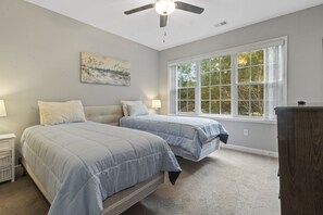 Ein Schlafzimmer mit zwei Betten, einem Deckenventilator, einem großen Fenster und einem Gemälde an der Wand.