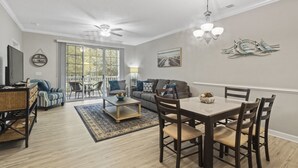 Ein geräumiges Wohnzimmer mit Essbereich, großen Fenstern, Deckenventilatoren und Blick ins Freie.