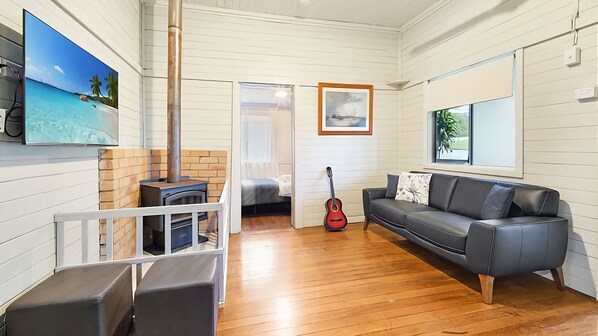 A cozy living room with a fireplace, a sofa, a guitar, and a painting of a beach scene. - Driftway is the ultimate family home in the beautiful seaside town of Urunga. (Urunga)