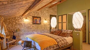 A cozy bedroom with a stone wall, a bed with plaid bedding, a bench, and a unique light fixture.